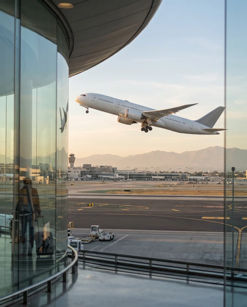 Commercial airplane taking off beside a modern airport terminal with mountains in the distance